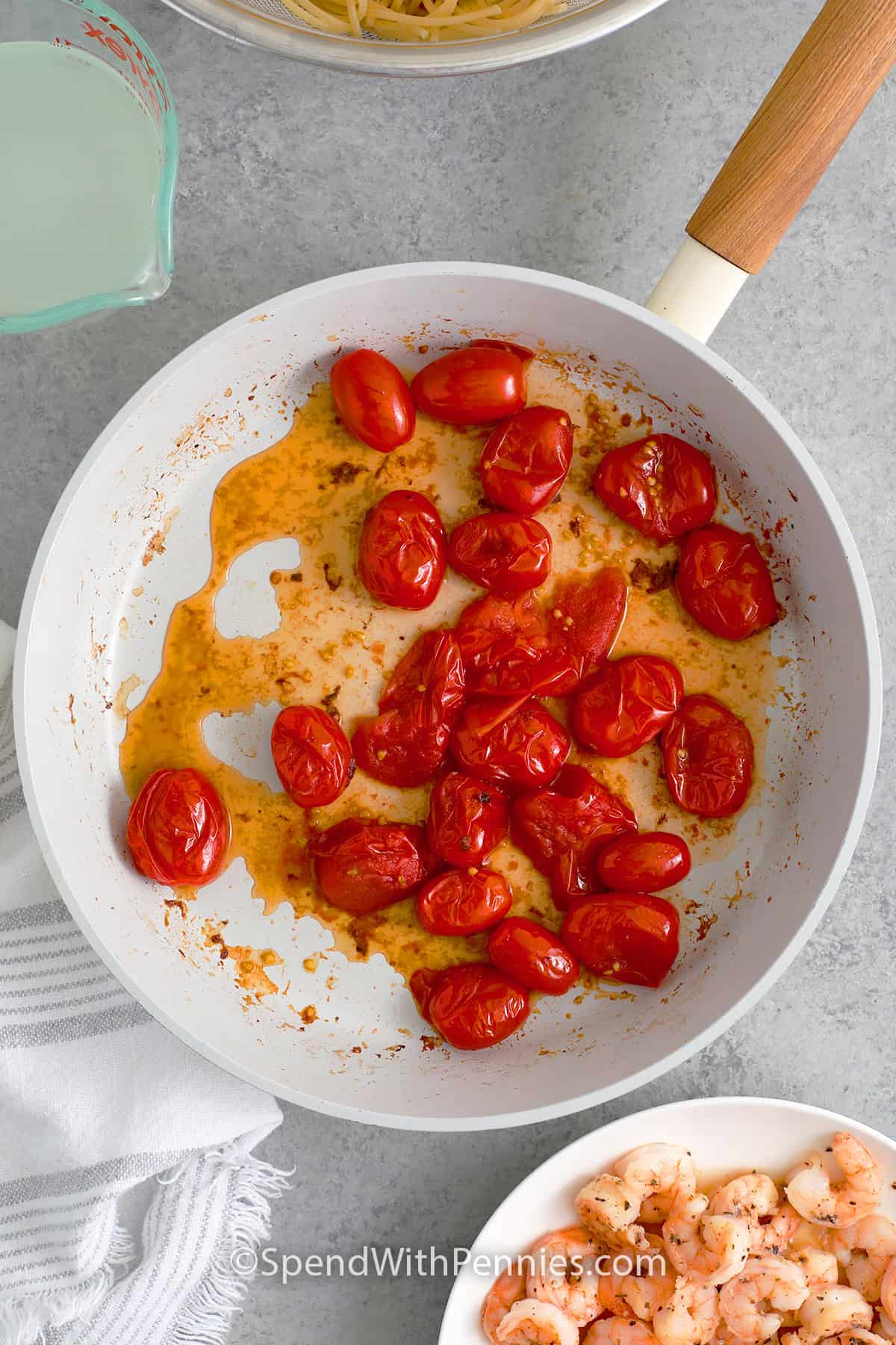 Burst cherry tomatoes cooking in a skillet to make Shrimp Pesto Pasta