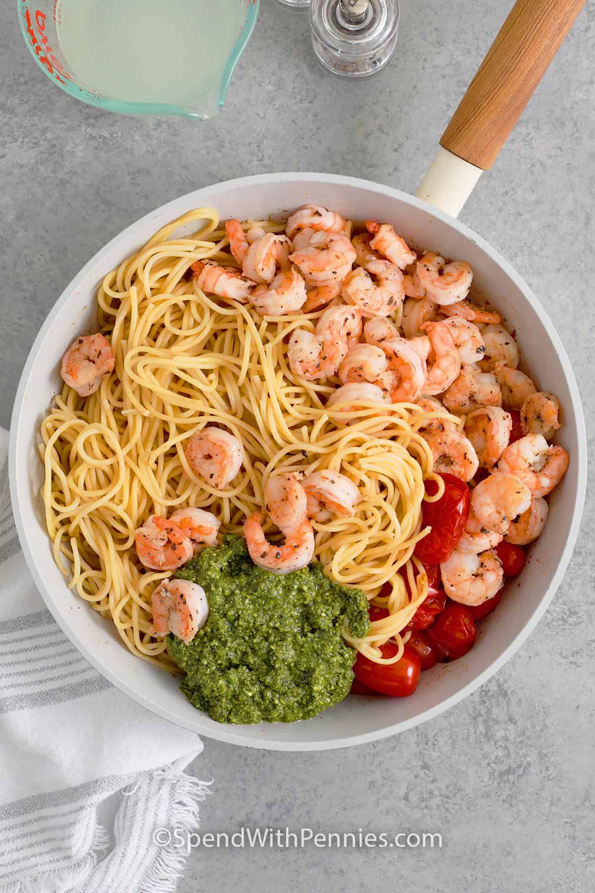 A skillet with cooked pasta and shimp, pesto, and cherry tomatoes about to be tossed together to make Shrimp Pesto Pasta