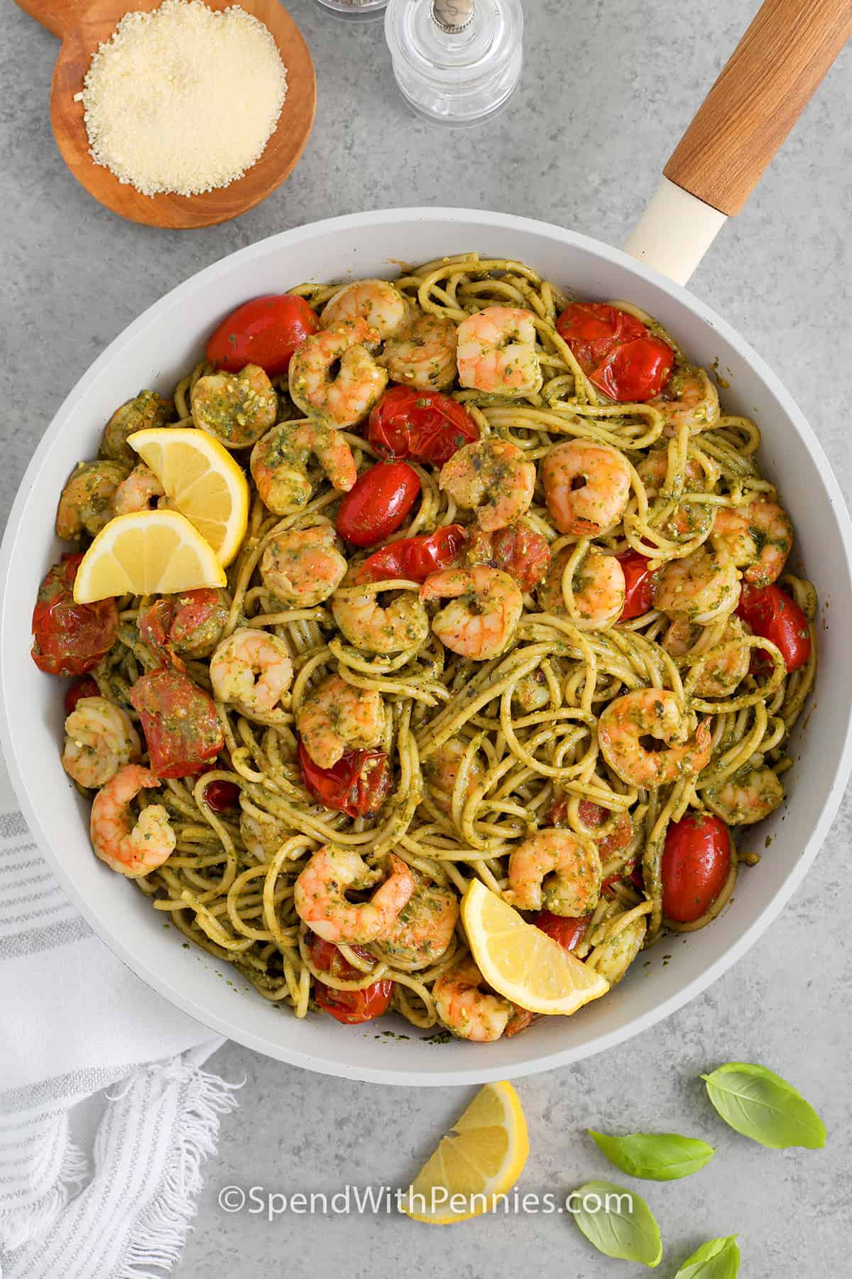 An overhead view of skillet of Shrimp Pesto Pasta garnished with lemon wedges and parmesan cheese