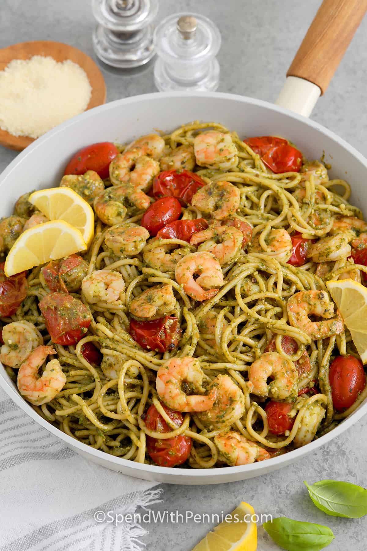 A skillet of Shrimp Pesto Pasta garnished with lemon wedges and parmesan cheese