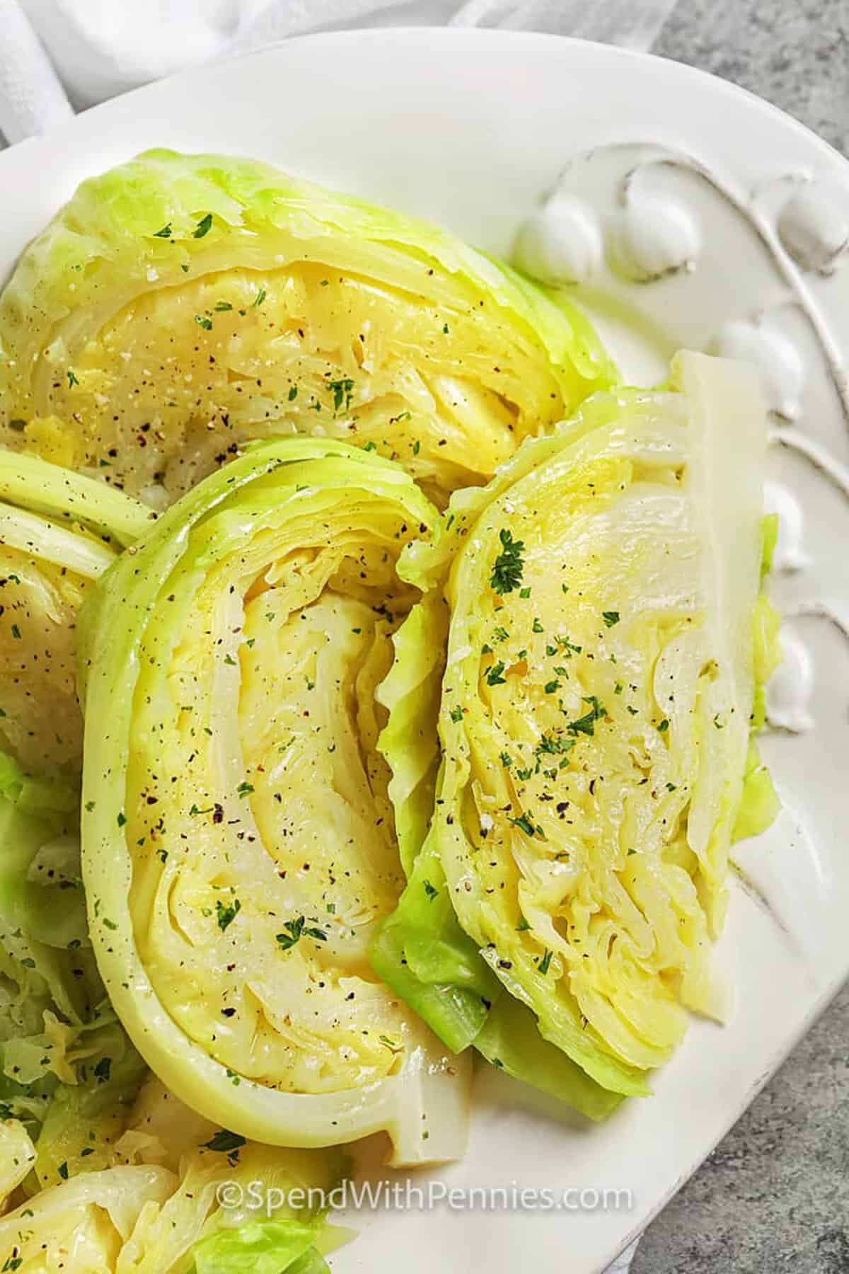This easy boiled cabbage recipe is a budget-friendly side dish that works for weeknights and holidays. Green cabbage boils until just tender, then drains well for the best texture. Finish with melted butter, salt, and black pepper for simple flavor that lets the cabbage shine. Use broth instead of water for extra savoriness, or top with bacon bits for a richer, more comforting plate. #spendwithpennies boiled cabbage wedges on a plate