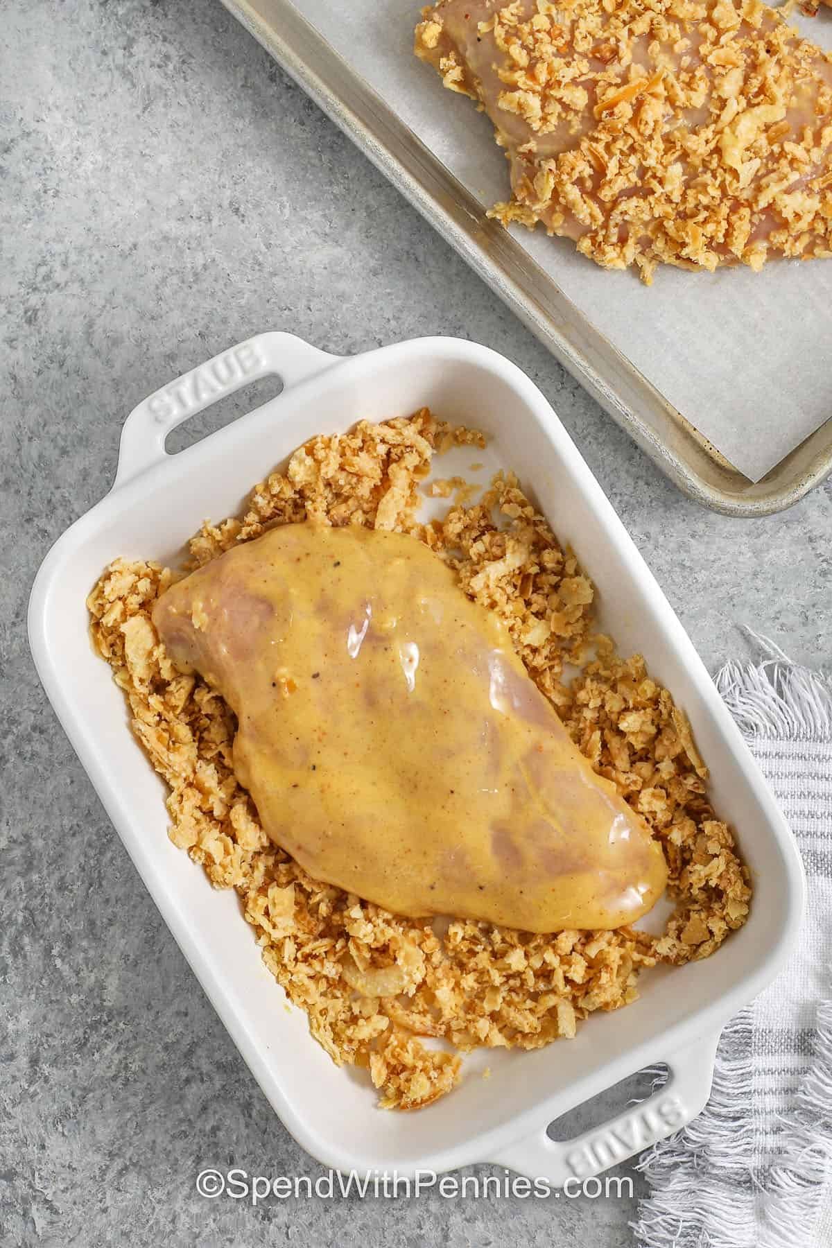 If you love crunchy chicken without frying, French onion baked chicken is a perfect fit. Crispy fried onions act like a seasoned coating, while Dijon adds a tangy flavor. Bake the coated chicken breasts on a sheet pan until golden and crispy. This crunchy French onion chicken pairs well with rice pilaf, green beans, or a simple salad. #spendwithpennies preparing french onion baked chicken coated in egg and pressed in onion mixture
