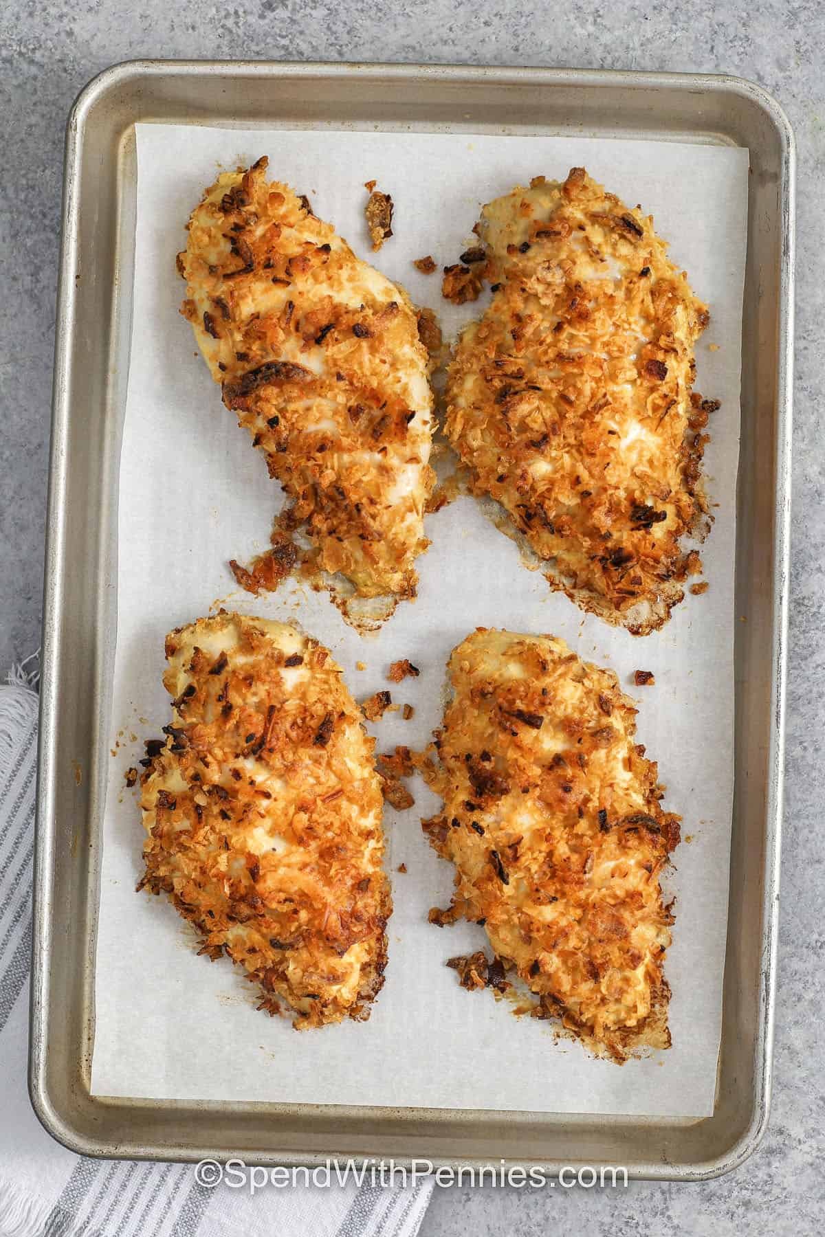 French onion baked chicken turns a few simple ingredients into a crispy, savory dinner. Crush the crispy fried onions so they cling better, then press them onto chicken breasts coated in egg and Dijon. Baking helps the chicken cook quickly and stay moist. If the topping browns early, tent lightly with foil and finish baking. Reheat leftovers in the oven to bring back the crunch. #spendwithpennies top view of french onion baked chicken on a pan