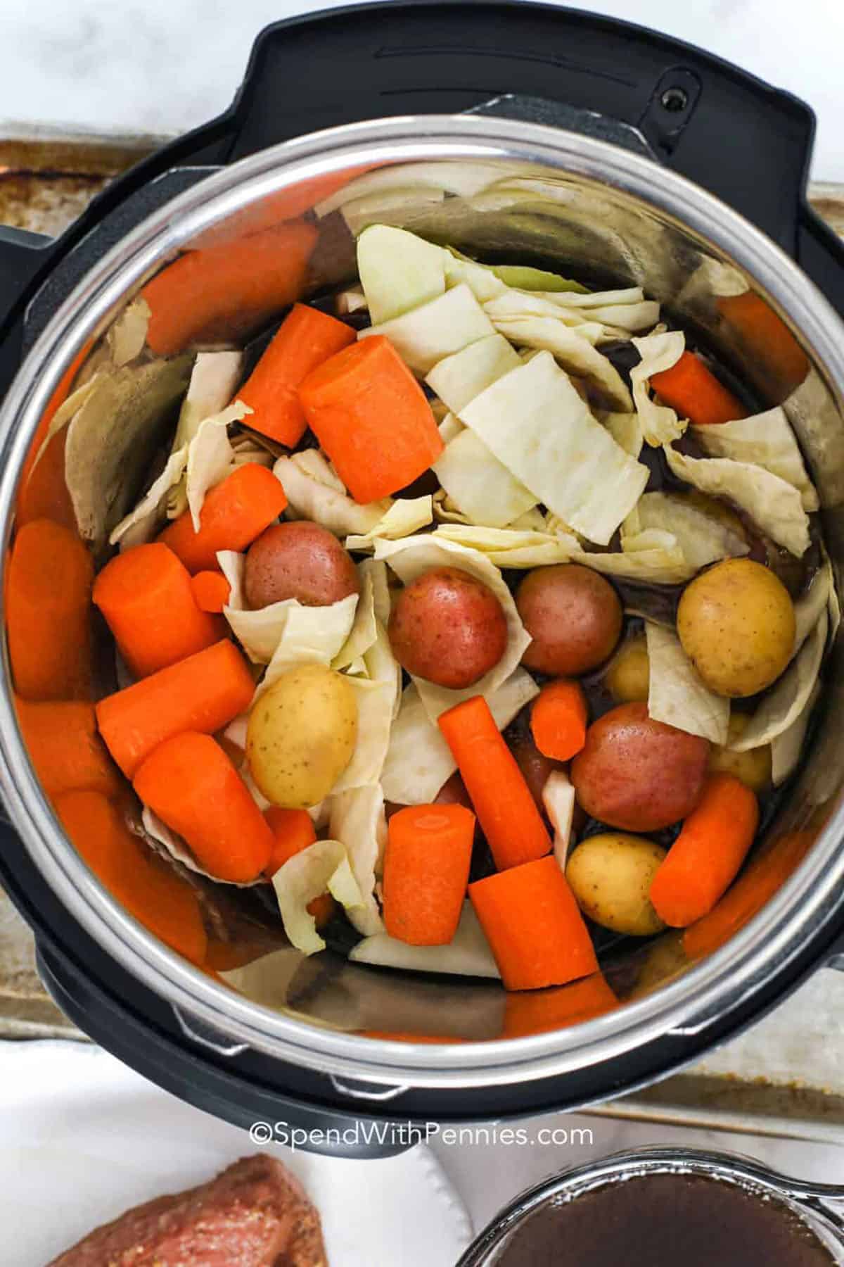 This Instant Pot corned beef and cabbage recipe delivers classic comfort with a simple, one-pot method. The corned beef brisket cooks on a trivet with garlic, onion, beer, and broth, then the cabbage, potatoes, and carrots finish in minutes. Slice across the grain for the most tender texture, and spoon a little pot liquid over the meat for extra moisture and flavor. #spendwithpennies adding potatoes annd vegetables to pot to make Instant Pot Corned Beef