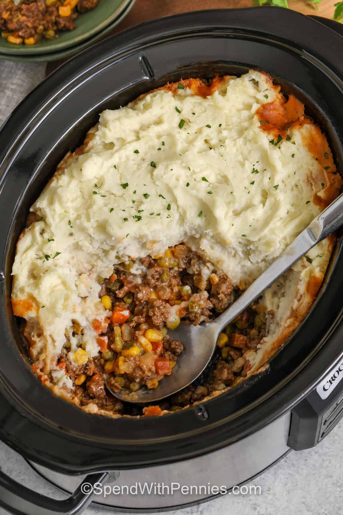Slow Cooker shepherd's pie is cozy comfort food with smart shortcuts. Frozen vegetables and gravy mix keep prep simple, while tomato paste and Worcestershire add rich, savory depth. Thick mashed potatoes warm through on top and create that classic shepherd’s pie finish. For the best texture, drain the browned meat well and rest the dish after cooking so the filling thickens before serving. #spendwithpennies Slow Cooker Shepherd's Pie in the pot with a spoon