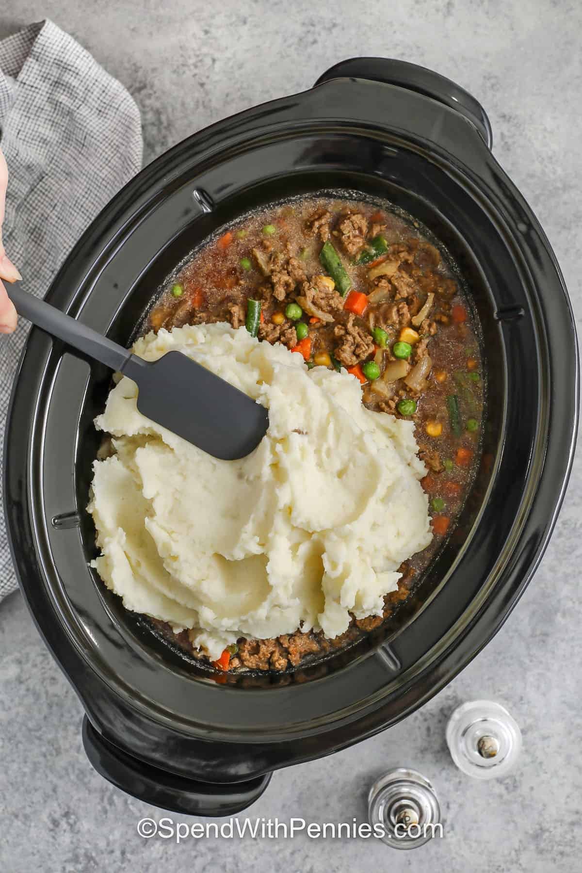 Make Slow Cooker shepherd's pie on busy days with frozen mixed vegetables and prepared mashed potatoes. Browning the meat first adds deeper flavor, then a quick gravy mix sauce with tomato paste and Worcestershire cooks into a savory filling. Spread thick mashed potatoes edge-to-edge so the topping stays fluffy. #spendwithpennies adding mashed potatoes on top of ingredients in slow cooker to make Slow Cooker Shepherd's Pie