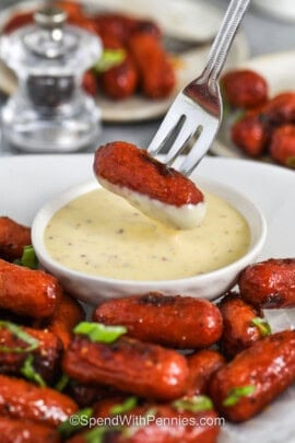 close up of dipping Sticky Honey Mustard Sausage in sauce