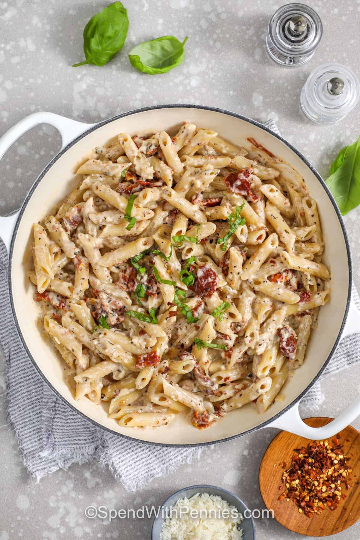 Make sun dried tomato pasta on rushed weeknights when you need a quick dinner. Garlic cooks briefly in the reserved tomato oil to build flavor, then half-and-half creates a creamy sauce with Parmesan cheese. Toss with penne, and adjust with pasta water until the sauce is smooth. Add spinach to wilt at the end or stir in chicken or grilled salmon for a heartier meal. #spendwithpennies overhead view of sun dried tomato pasta with basil garnish and parmesan, chili flakes, salt and pepper in background