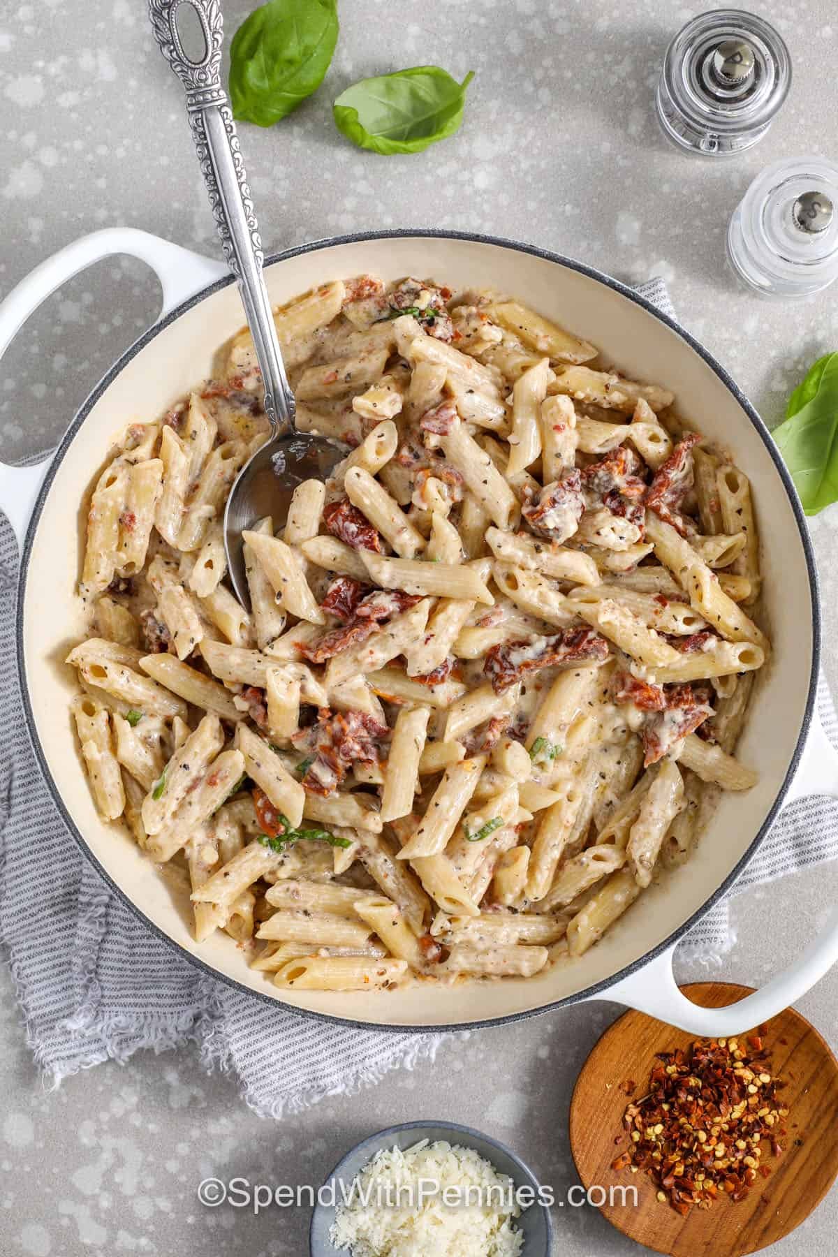 This sun dried tomato pasta recipe makes a smooth cream sauce that’s ready in under 30 minutes. Oil-packed sun-dried tomatoes bring bold, sweet-tangy flavor, while dried basil and oregano add warmth. Whisk half-and-half with cornstarch for quick thickening, then melt in Parmesan and toss with penne. Add pasta water a little at a time for a smooth, creamy sauce that tastes restaurant-quality at home. #spendwithpennies top view of finished sundried tomato pasta with parmesan, chili flakes, basil, and salt and pepper