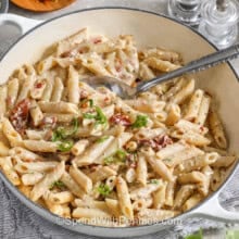 closeup of a serving bowl of sun dried tomato pasta with a serving spoon