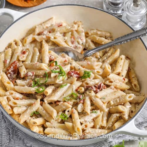 closeup of a serving bowl of sun dried tomato pasta with a serving spoon