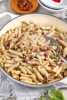a serving bowl of sun dried tomato pasta with dried chili flakes in the background