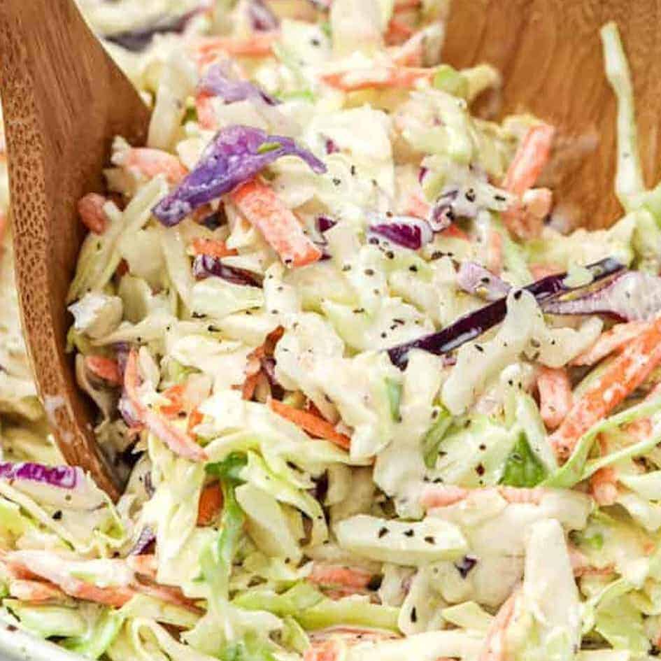 A prepared Coleslaw recipe in a bowl with two wooden serving spoons