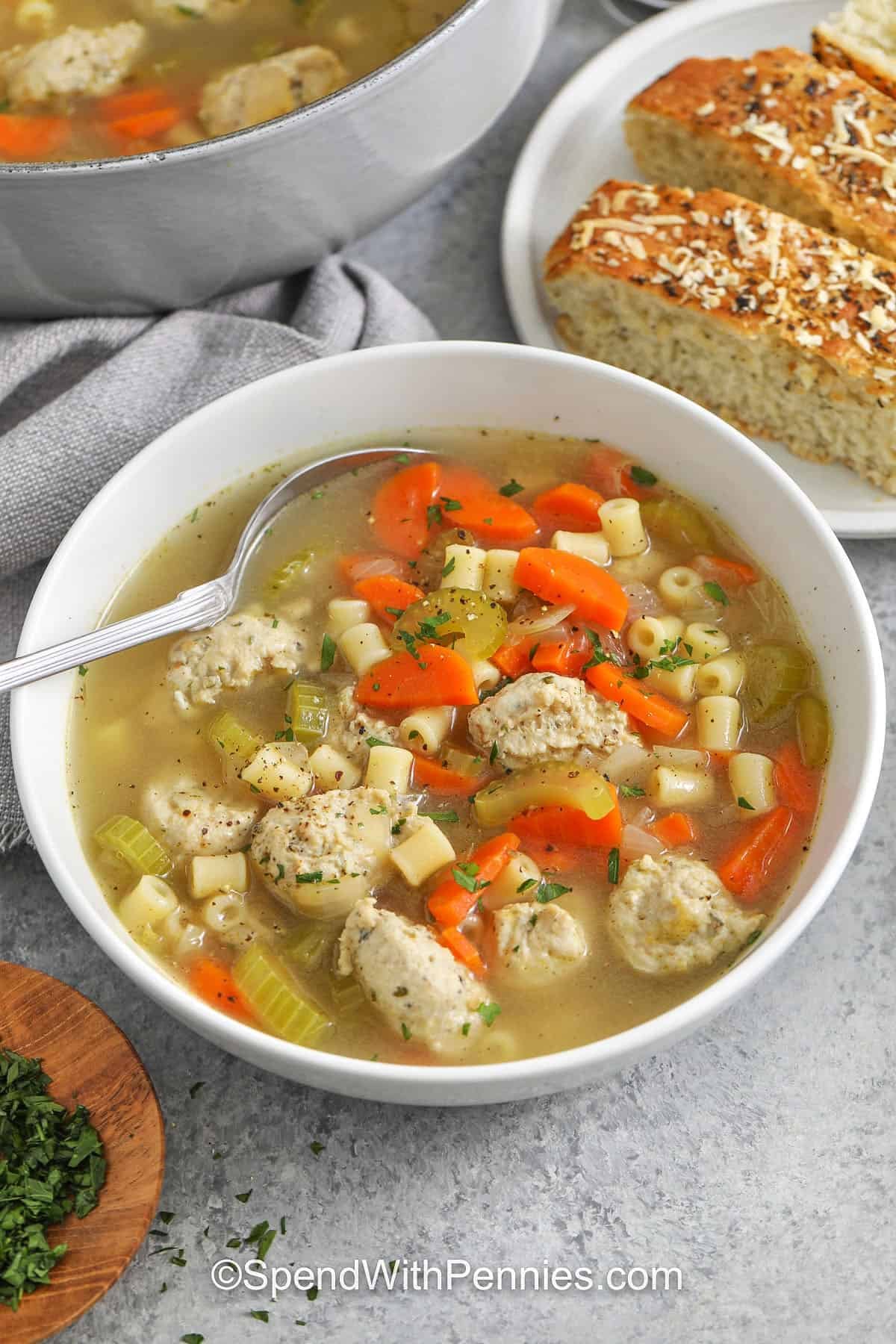 bowl of savory Chicken Meatball Soup with a plate of bread beside it and pot in the back