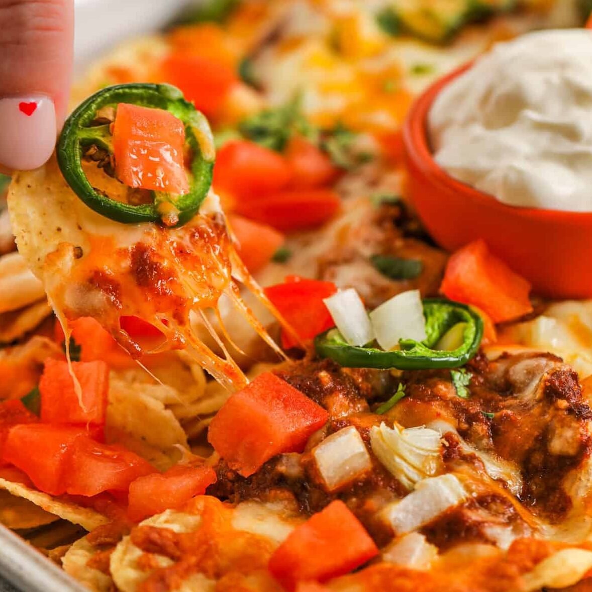 taking a chip with melted cheese from pan of Chili Nachos
