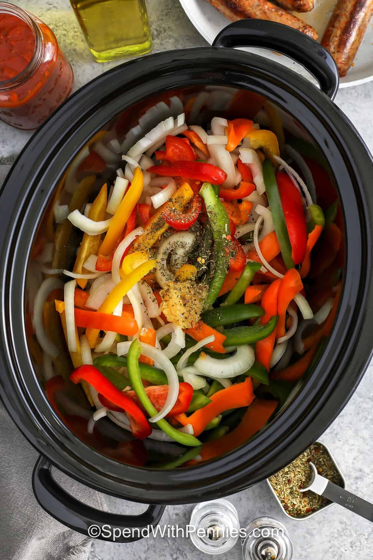 adding bell peppers , onion with garlic and seasonings to slow cooker to make Slow Cooker Sausage and Peppers