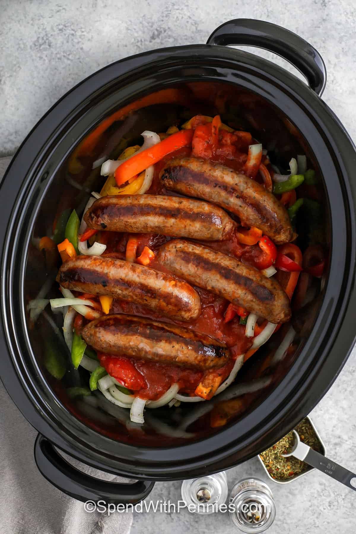 adding sauce and cooked sausages to slow cooker to make Slow Cooker Sausage and Peppers