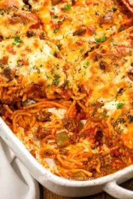 A pan of baked spaghetti with a piece missing so you can see the noodles under the cheese.
