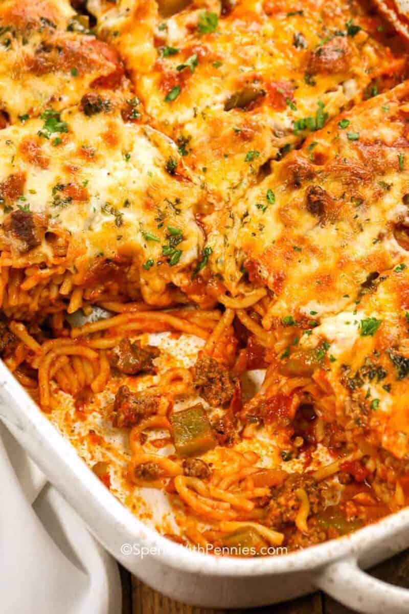 A pan of baked spaghetti with a piece missing so you can see the noodles under the cheese.