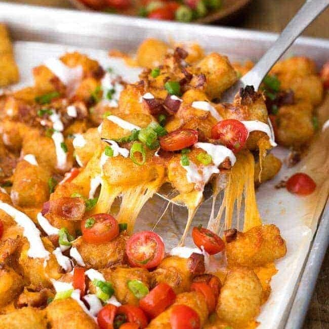 serving up Tater Tot Nachos garnished with green onion and tomatoes, from a baking tray