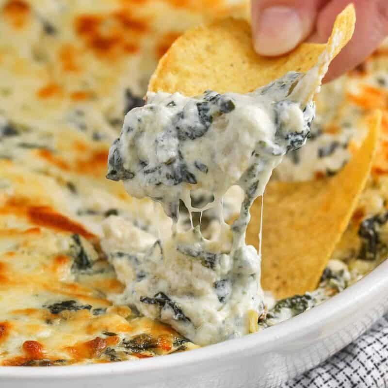 dipping a chip in The Best Spinach Artichoke Dip