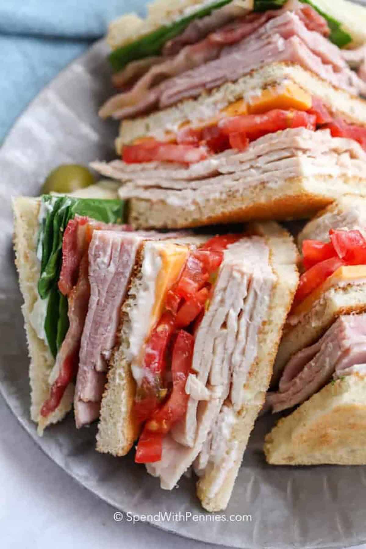 A classic club sandwich brings diner-style comfort with simple ingredients like turkey, ham, bacon, cheddar, tomato, and romaine lettuce. Toasted bread adds crunch, and mayonnaise helps keep the layers together for a less messy bite. This recipe is quick to assemble and easy to scale for a crowd. Prep the bacon ahead to make lunchtime even faster and keep the texture extra crisp. #spendwithpennies plated club sandwich