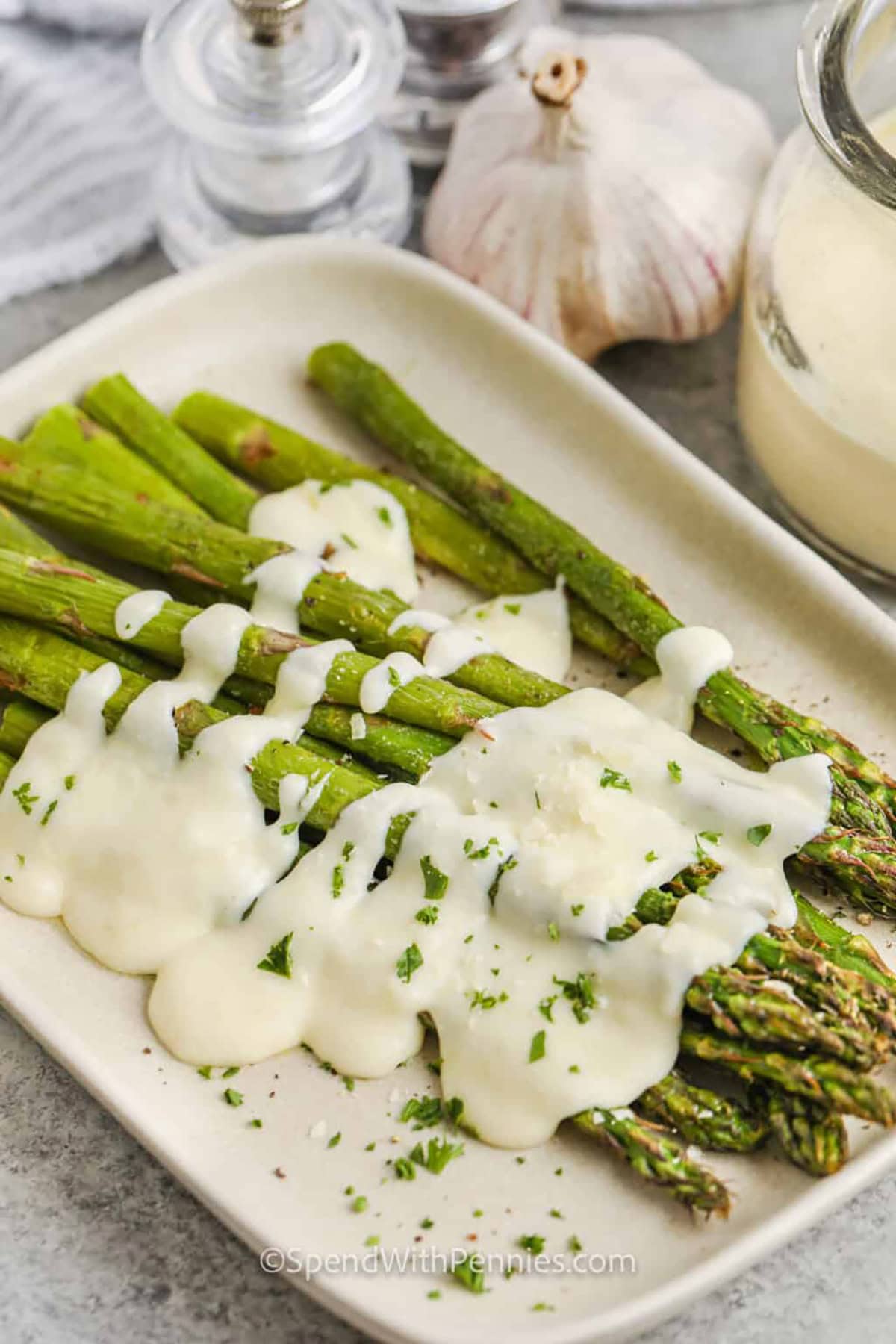 Garlic cream sauce poured over roasted asparagus on a plate