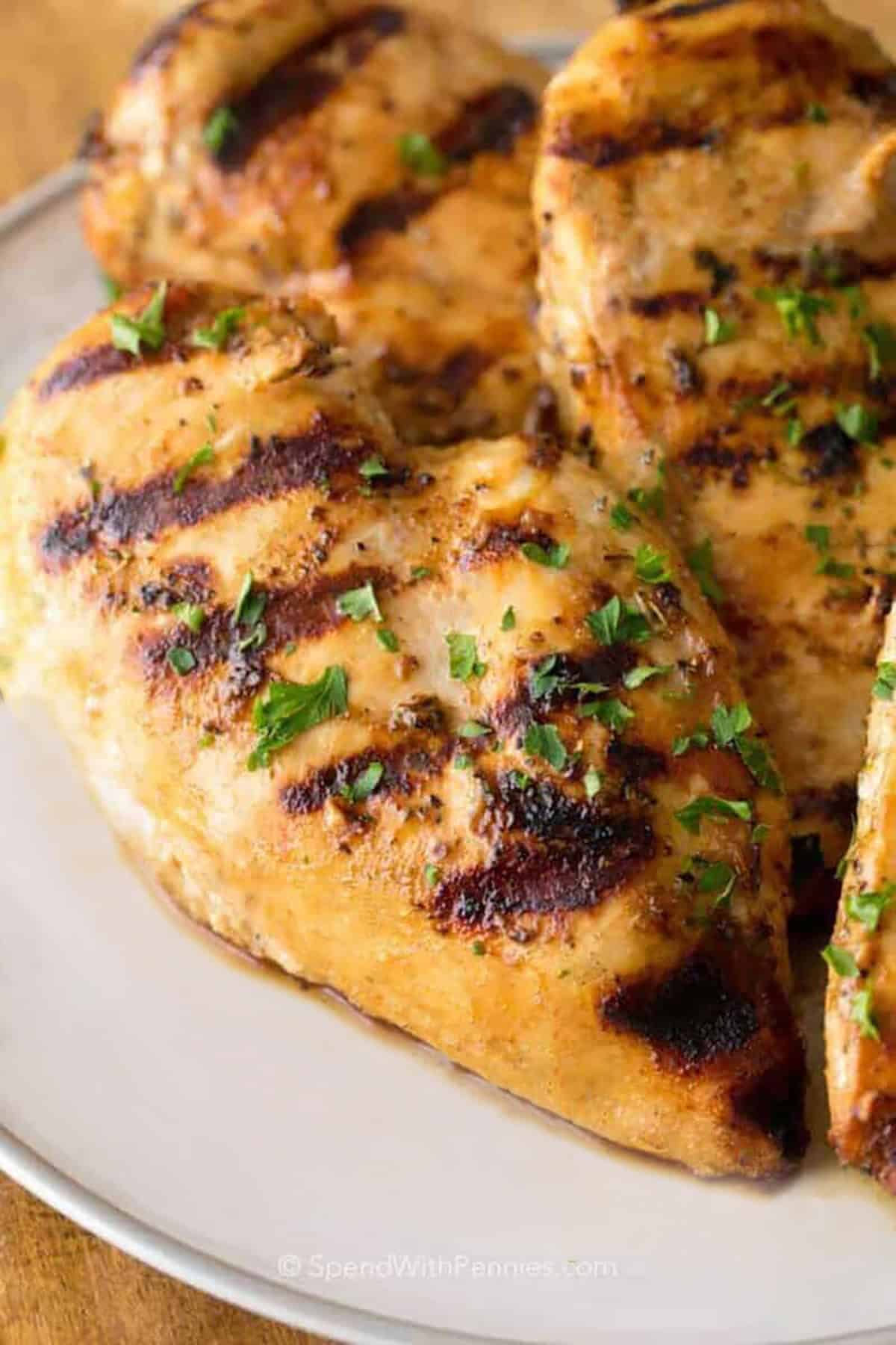 This grilled chicken breast recipe delivers tender slices with plenty of flavor and very little fuss. The marinade combines lemon juice, Dijon, oil, and Italian seasoning to keep the chicken moist and well seasoned while it cooks. Serve it with grilled vegetables or rice, then use any extras in chicken salad, quesadillas, or sandwiches the next day. #spendwithpennies grilled chicken on a white plate