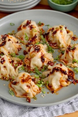 blanket dumplings on a plate with chili oil and green onions on top