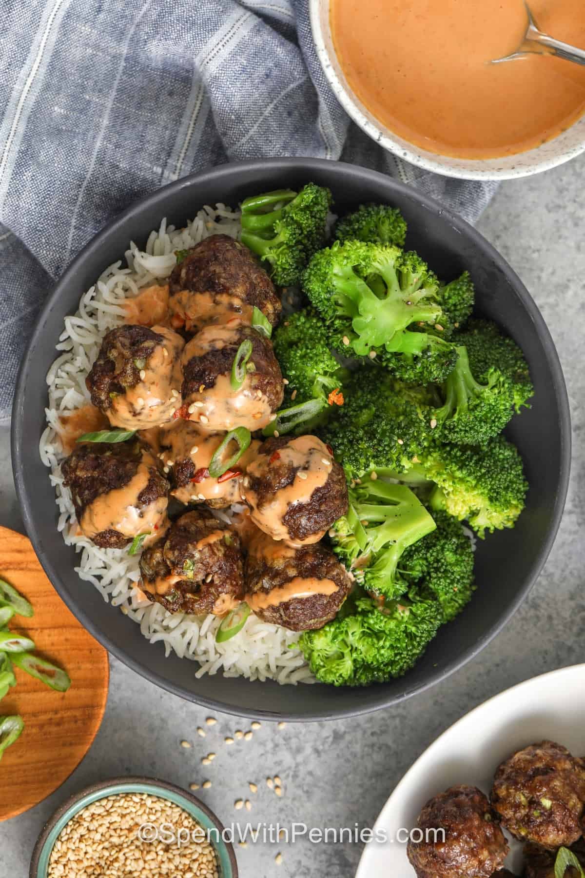 Firecracker meatballs are perfect for parties because they hold well and the sauce can be served on the side for dipping. The baked meatballs are seasoned with garlic and ginger, and the firecracker sauce is creamy and spicy with sriracha, honey, soy sauce, and red pepper flakes. Add sesame oil for a toasty finish and garnish with green onions for a bright pop. #spendwithpennies firecracker meatballs in a bowl with broccoli and rice