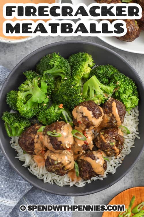 Firecracker meatballs are tender baked beef meatballs seasoned with ginger, garlic, and green onion, then drizzled with a creamy sriracha mayo firecracker sauce. The sauce is sweetened with honey and balanced with soy sauce for a savory finish. Serve over rice, in lettuce wraps, or as an appetizer with extra sauce for dipping. #spendwithpennies firecracker meatballs in a bowl with writing