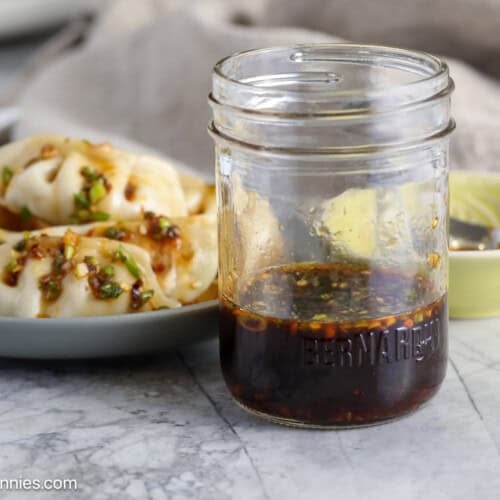 A jar of dumpling sauce next to a plate of dumplings