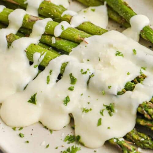 Close up of Garlic cream sauce poured over roasted asparagus on a plate