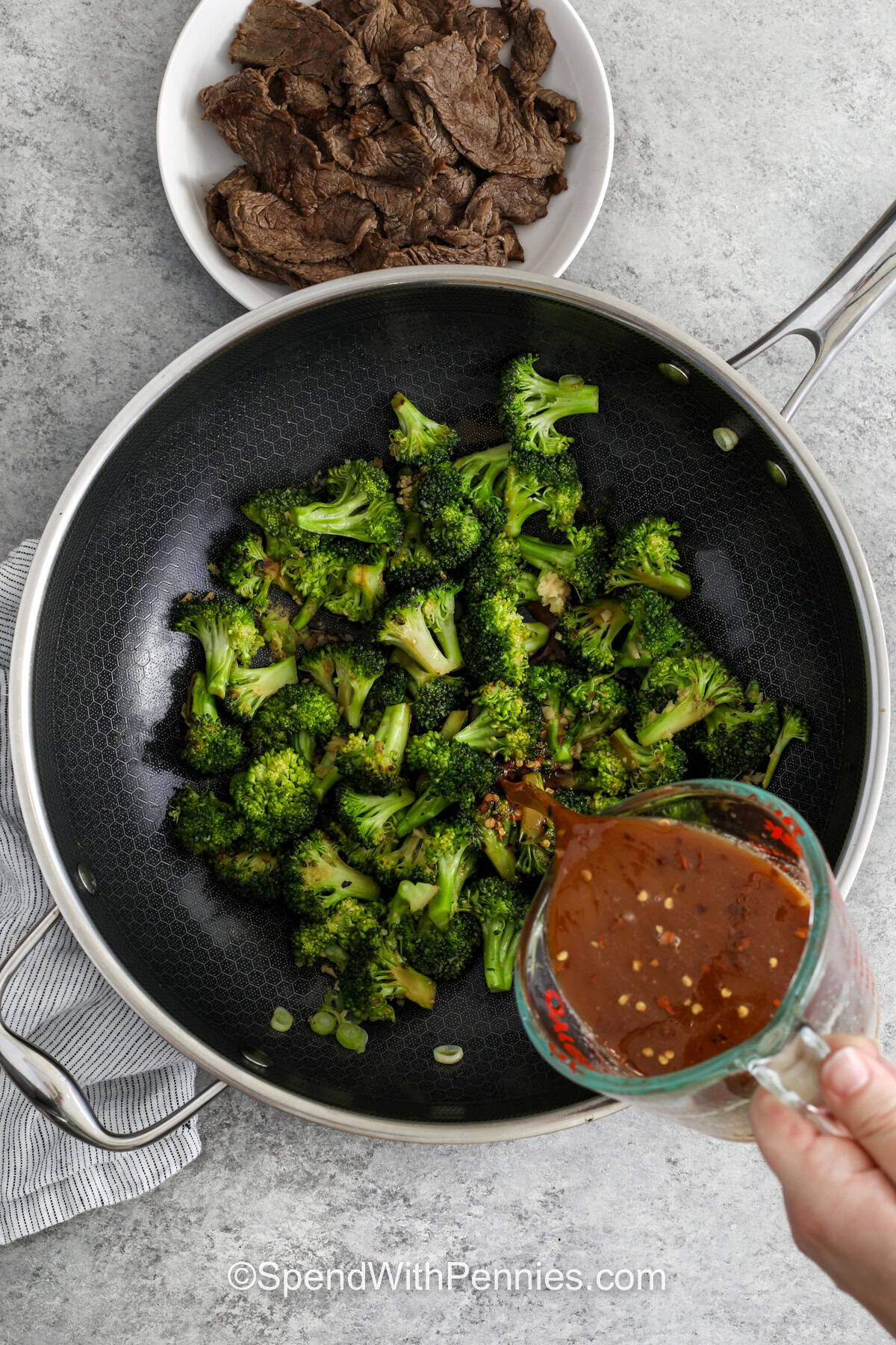 This easy beef and broccoli recipe is packed with flavor from soy sauce, toasted sesame oil, garlic, and ginger, all simmered into a silky sauce. The steak stays tender when sliced thinly across the grain, and the broccoli catches all that savory glaze. It is a practical dinner idea for anyone who wants a homemade meal that is fast, cozy, and worth saving. #spendwithpennies adding sauce to broccoli to make Beef and Broccoli Recipe