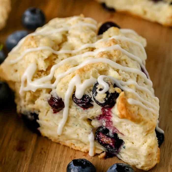 a blueberry scone with drizzle on a wood cutting board