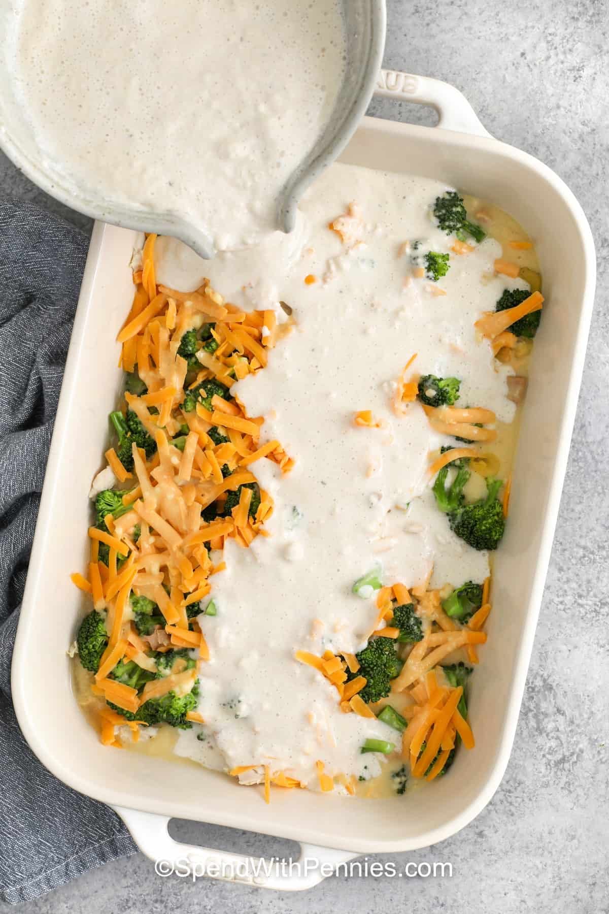 adding cream mixture to broccoli and cheese in dish to make Cheddar Chicken Cobbler
