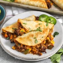 crispy tacos on a white plate with peppers and cilantro