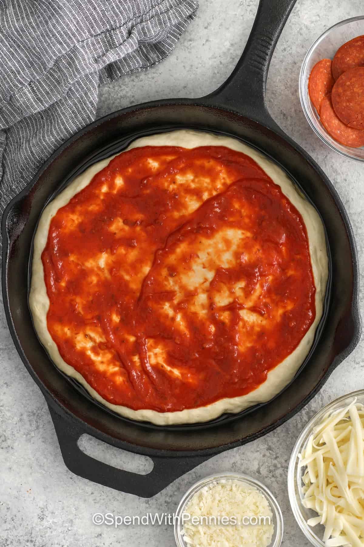 Pan pizza is a smart choice when you want a homemade dinner that feels fun but does not take much effort. Baking the dough in a cast iron skillet gives it a chewy center and crisp outer crust, while pizza sauce, mozzarella, and pepperoni keep the toppings classic and easy to love. This is the kind of recipe that feels low-stress, budget-friendly, and always welcome at the table. #spendwithpennies adding pizza sauce to pizza dough to make Homemade Pan Pizza
