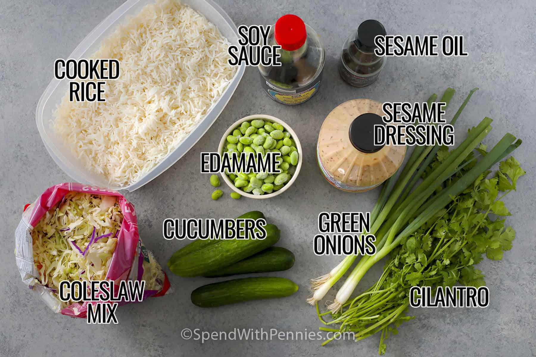 Rice, coleslaw mix, soy sauce, sesame oil, sesame dressing, edamame, mini cucumbers, green onions and cilantro laid out and labeled to make Crispy Rice Salad.