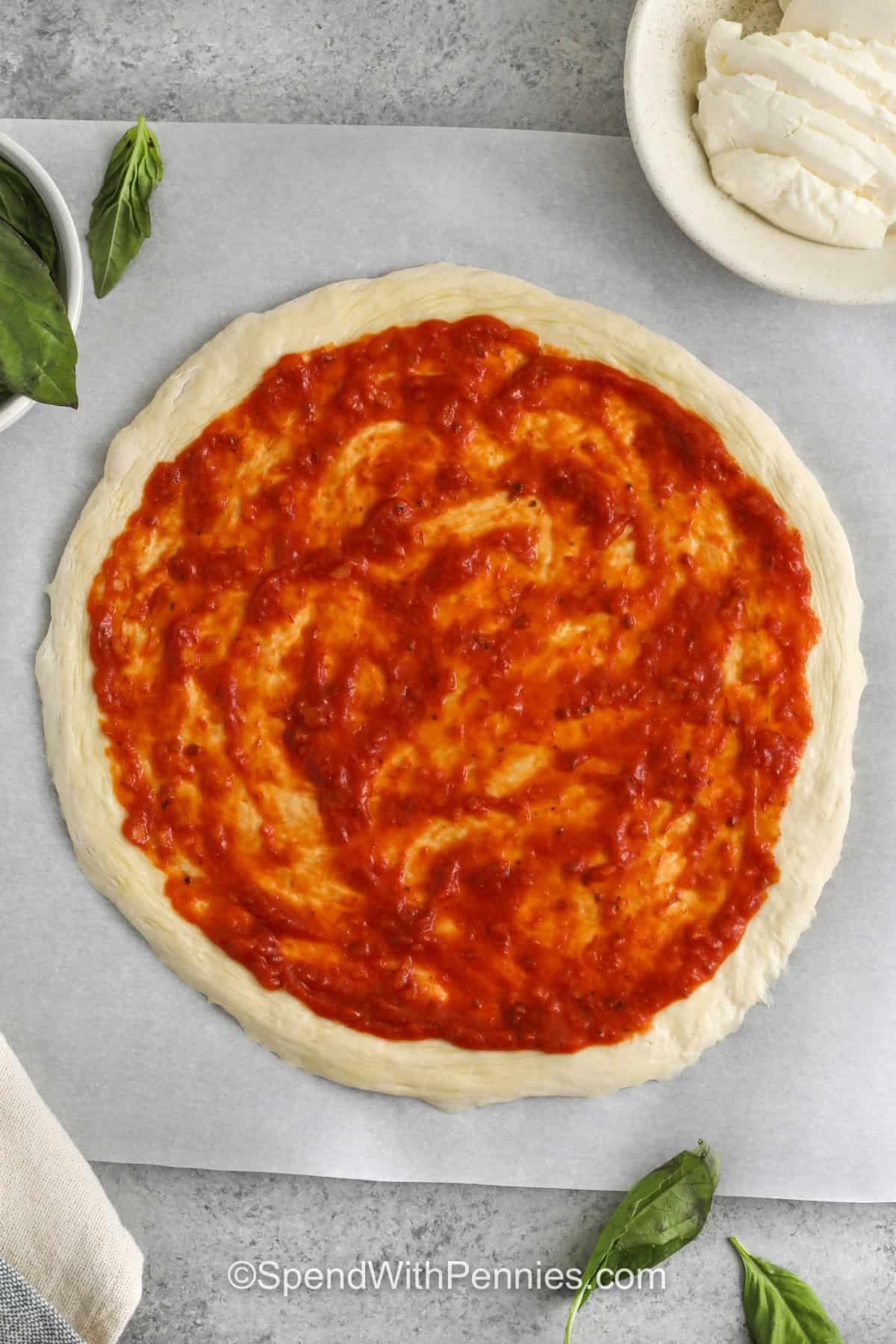 adding pizza sauce to pizza crust to make Margherita Pizza