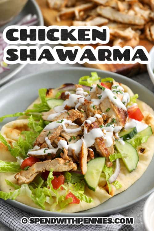 Homemade chicken shawarma is a flavorful oven-baked chicken recipe with juicy slices and crisp edges. The marinade uses plain yogurt, fresh lemon juice, garlic, and shawarma seasoning to tenderize the chicken and add warm, savory flavor. Serve it with rice, pitas, fresh vegetables, and a creamy white sauce for an easy dinner that feels fresh, filling, and family-friendly. #spendwithpennies Chicken Shawarma wrap on a plate with cutting board of chicken slices and a title