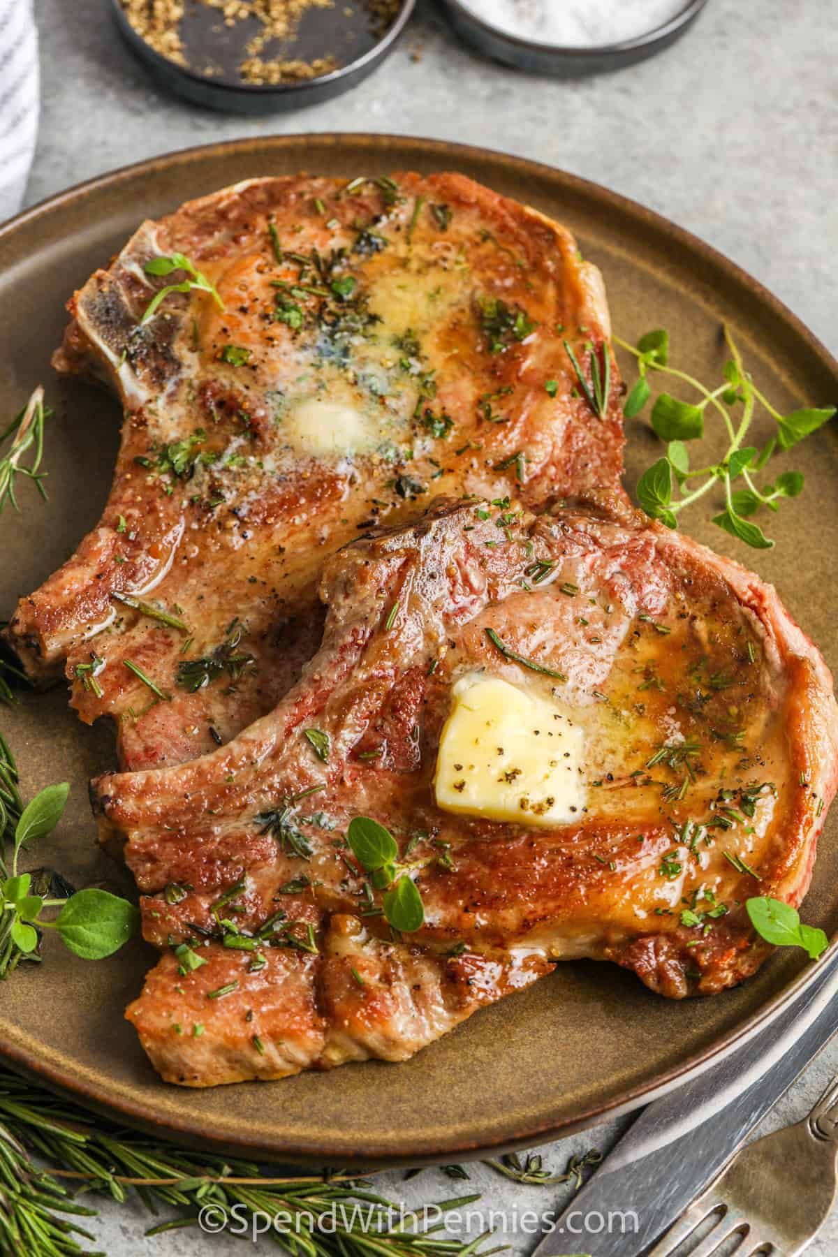 Pan seared pork chops get beautifully browned and stay tender with this easy skillet method. The pork is seared first for a crisp crust, then cooked to temperature and rested so the juices stay inside. Thyme, rosemary, butter, and optional garlic make a simple pan sauce that tastes rich and cozy. Make these pan seared chops with creamy mashed potatoes, roasted vegetables, or a fresh green salad. #spendwithpennies plated Pan Seared Pork Chops with melted butter