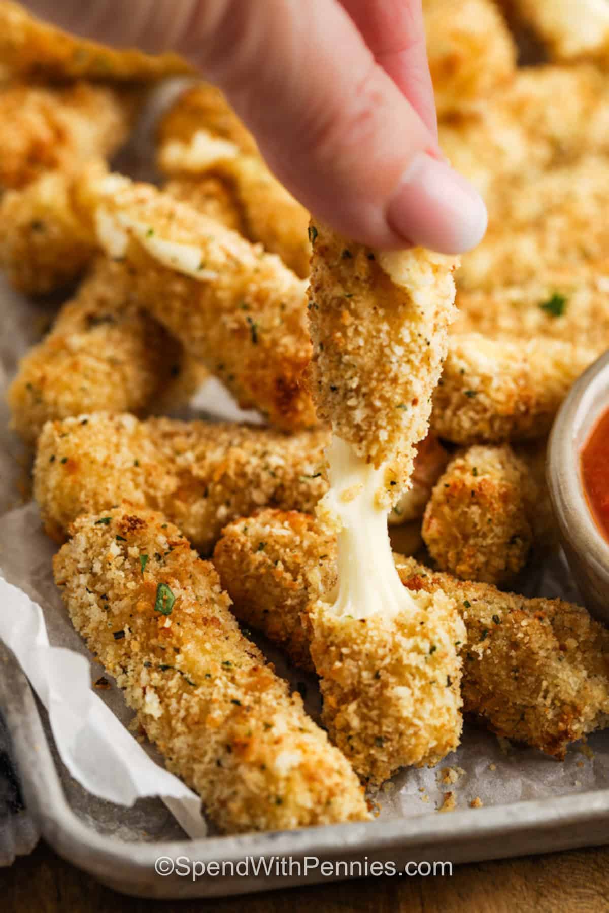 baking sheet with Air Fryer Mozzarella Sticks with someone breaking apart one to show cheesy filling