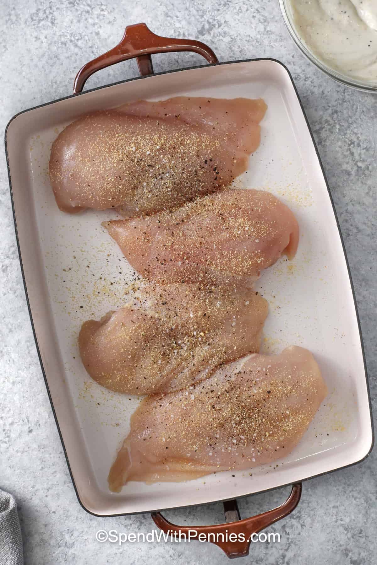 This Caesar chicken recipe is an easy baked chicken dinner made with boneless chicken breasts, Caesar dressing, sour cream, Italian cheese, and crushed croutons. The creamy sauce keeps the chicken tender while the buttery topping bakes up golden and crisp. Serve this cozy one-dish meal for busy weeknights. #spendwithpennies adding seasonings to chicken to make Caesar Chicken Recipe
