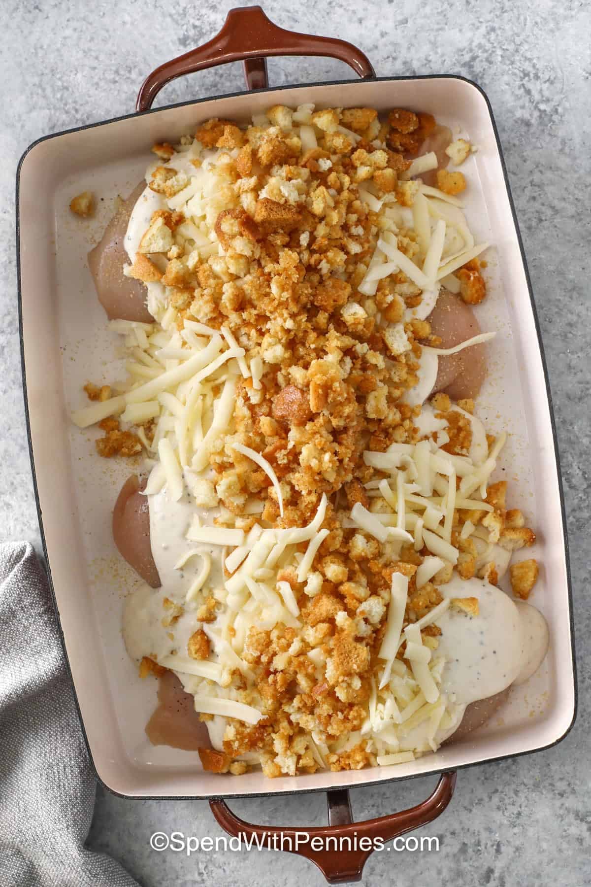 This baked Caesar chicken recipe is a warm and comforting twist on classic Caesar flavors. Creamy Caesar dressing, tangy sour cream or Greek yogurt, shredded Italian cheese, and garlicky croutons make simple chicken breasts taste rich and savory. Serve this easy Caesar chicken with a crisp green salad, buttered noodles, roasted broccoli, or garlic bread for a family-friendly dinner. #spendwithpennies adding ingredients to dish to make Caesar Chicken Recipe