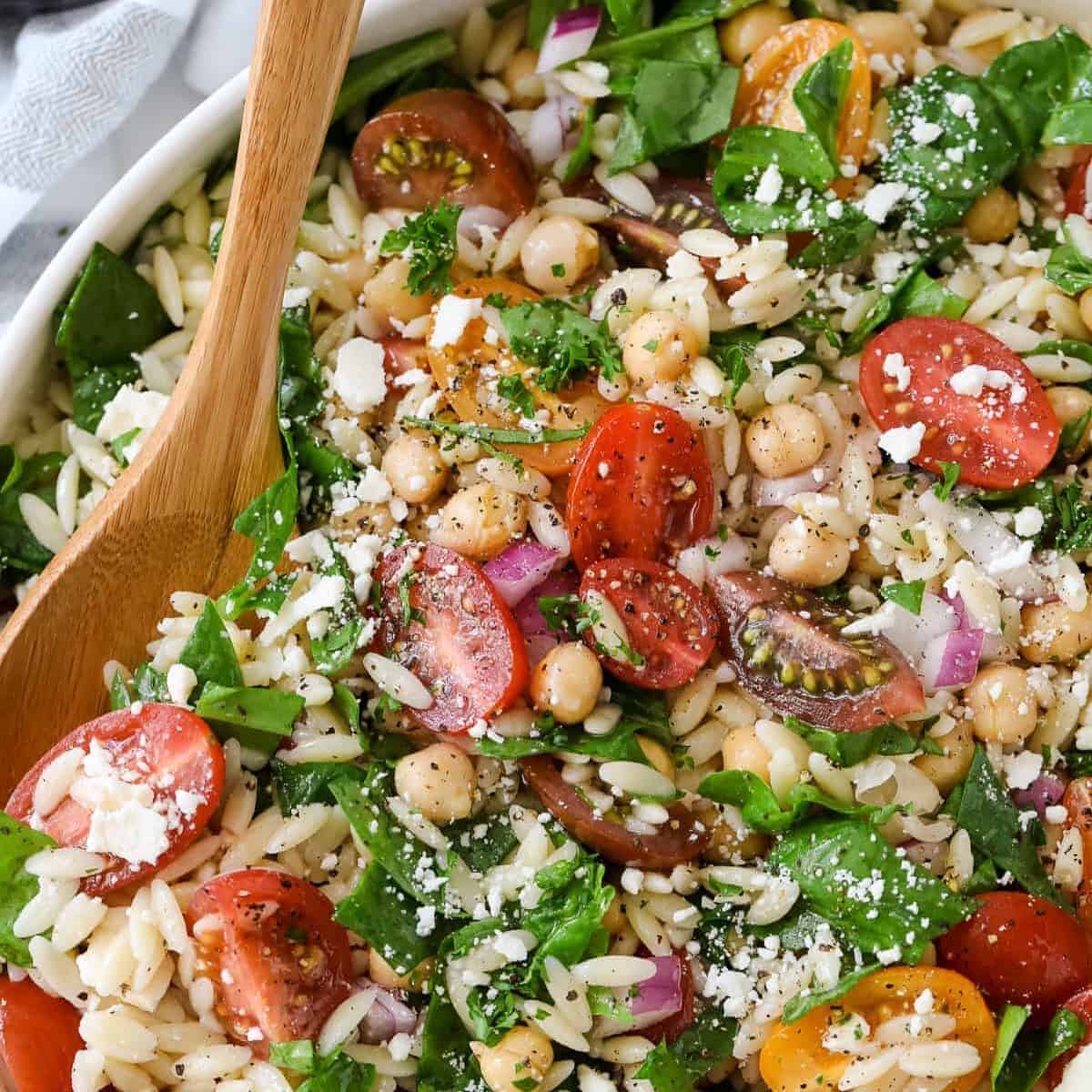 serving orzo pasta salad with a wooden spoon