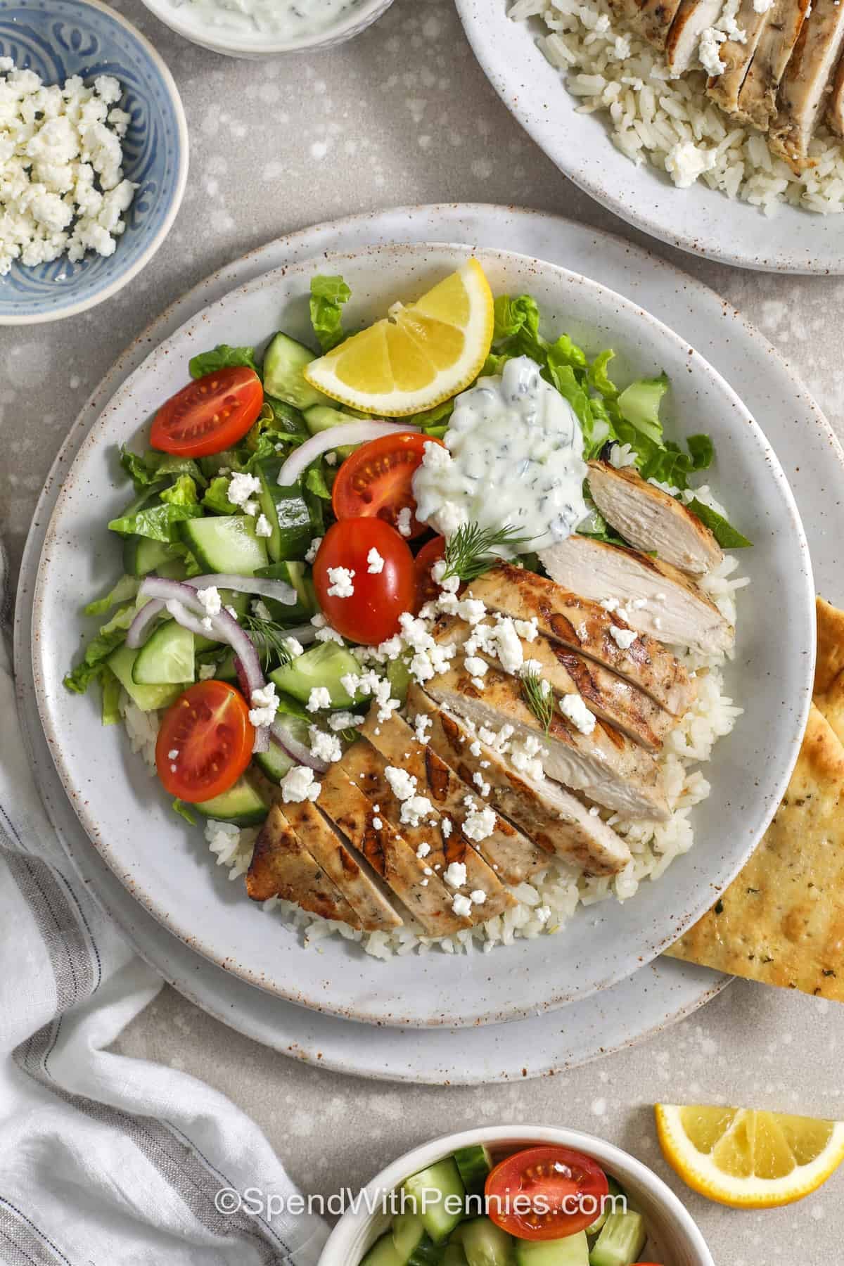 These Mediterranean Greek chicken bowls are fresh, bright, and easy to make with simple pantry ingredients. The chicken is cooked in a skillet until juicy, then served over herbed rice with tzatziki and Greek-style toppings. They are perfect for using up cucumbers, tomatoes, red onion, feta, and olives, and they can be made with rice, quinoa, or cauliflower rice. Make them for dinner or a light lunch. #spendwithpennies top view of Greek Chicken Bowls