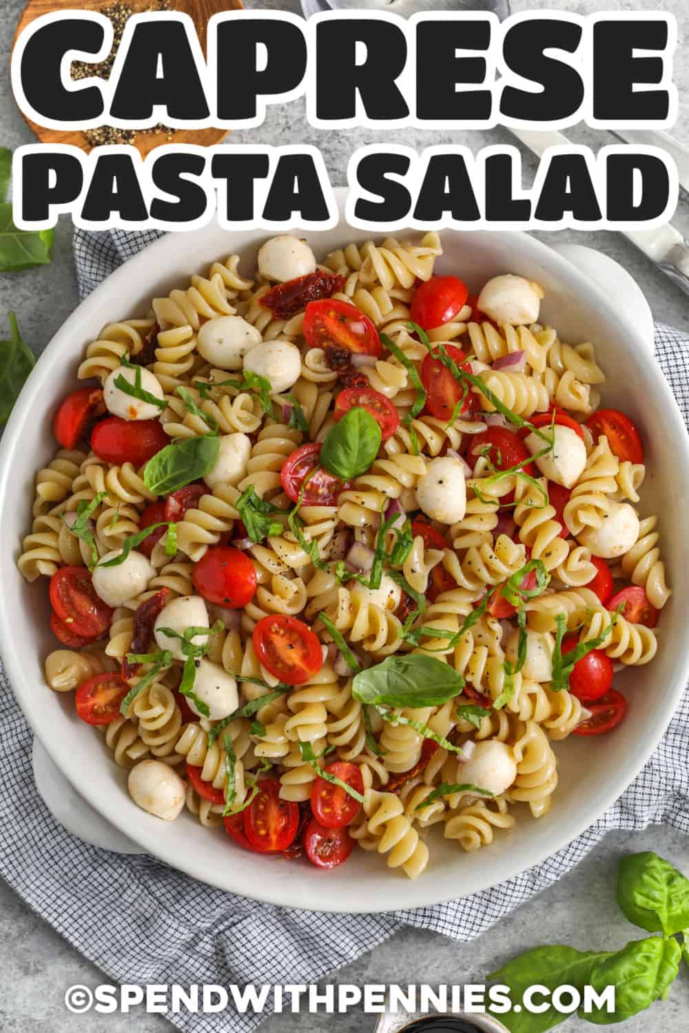 Caprese pasta salad is a fresh and colorful summer side dish made with rotini, grape tomatoes, mozzarella pearls, sun-dried tomatoes, basil, and a tangy red wine vinaigrette. It chills well before serving, making it a great make-ahead recipe for BBQs, picnics, potlucks, and easy family dinners. Add the drizzle of balsamic glaze for a sweet-tangy finish that brings out the tomato and basil flavors. #spendwithpennies plated Caprese Pasta Salad with writing