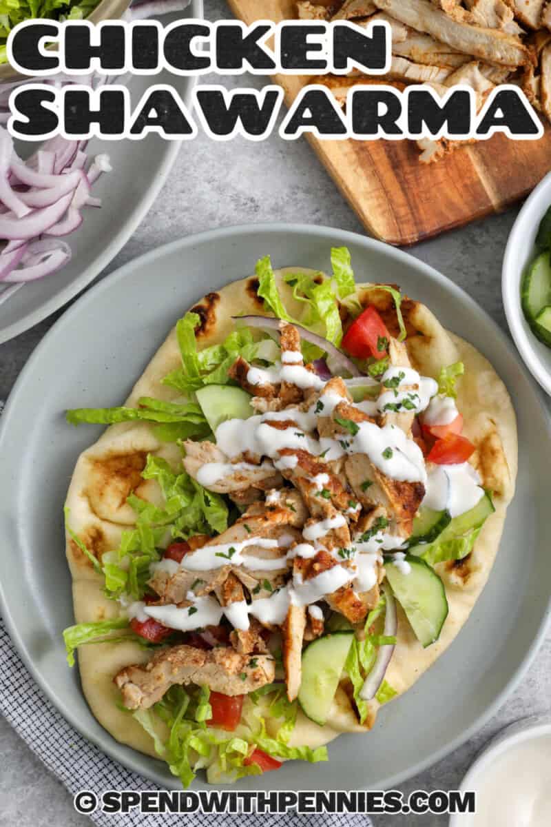 Homemade chicken shawarma is a flavorful oven-baked chicken recipe with juicy slices and crisp edges. The marinade uses plain yogurt, fresh lemon juice, garlic, and shawarma seasoning to tenderize the chicken and add warm, savory flavor. Serve it with rice, pitas, fresh vegetables, and a creamy white sauce for an easy dinner that feels fresh, filling, and family-friendly. #spendwithpennies Chicken Shawarma wrap on a plate with cutting board of chicken slices and a title