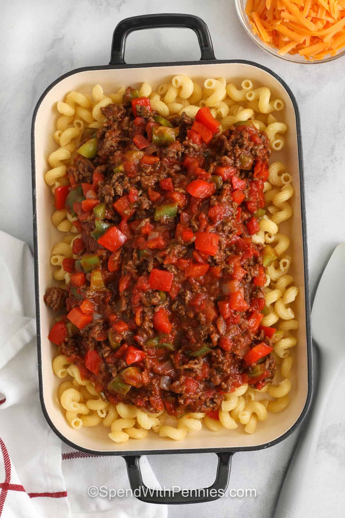 adding pepper and beef sauce to noodles to make Sloppy Joe Casserole